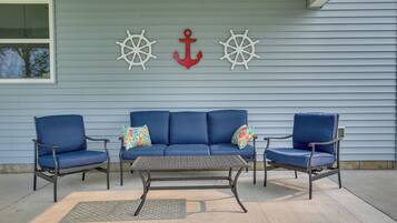 A blue outdoor seating area with a metal table and two blue chairs, a red anchor, and two ship wheels on the wall.