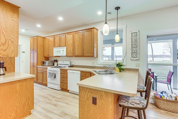 A modern kitchen with wooden cabinets, a central island, and a view of the outdoors. - Stunning Waterville Home on Tetonka Lake! (Waterville)
