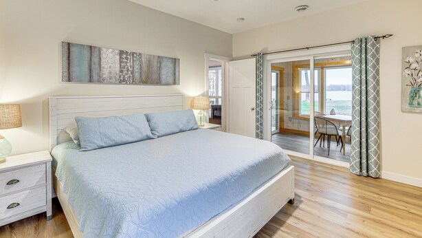 Ein Schlafzimmer mit Bett, Nachttischen, Deckenventilator und Blick durch eine Glastür in einen Außenbereich.
