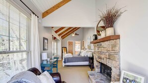 A cozy bedroom with a stone fireplace, a large bed, and a view of the adjacent living room.