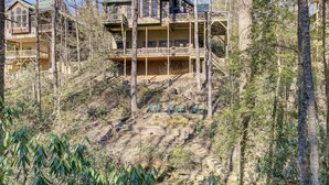 A large, multi-story house with a balcony and a staircase leading up to it, surrounded by trees.
