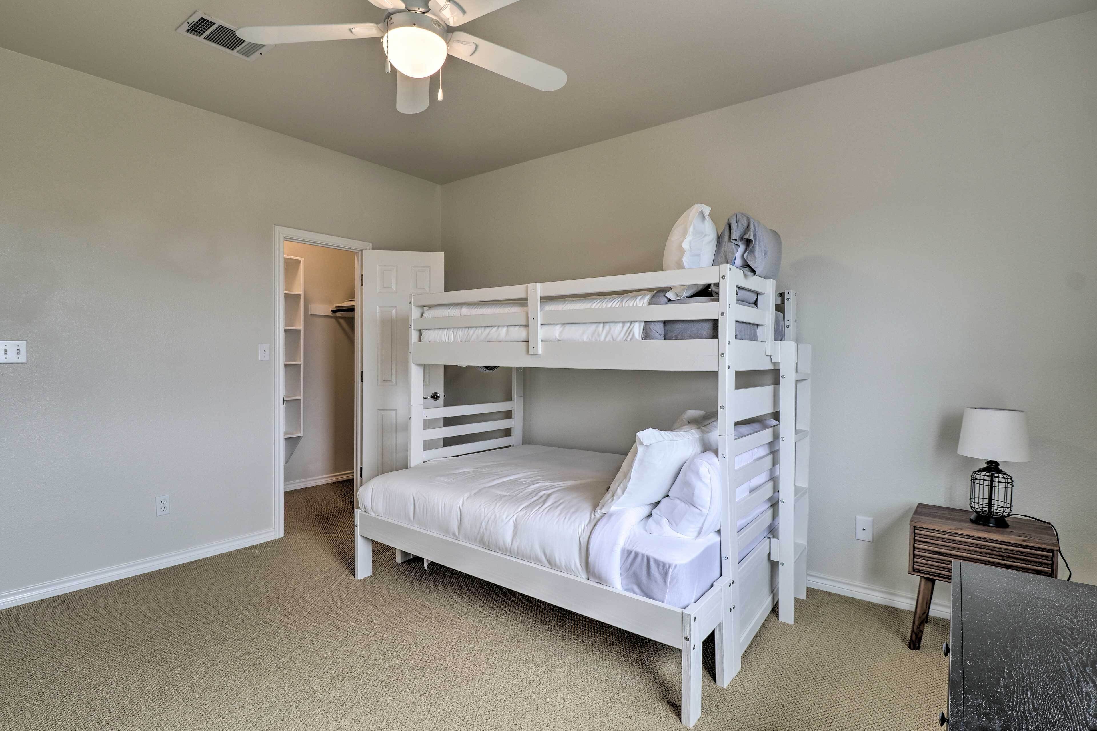 A bunk bed room with a ceiling fan, a bedside table with a lamp, and a closet with shelves.
