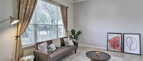 Sala de estar com sofá, mesa de centro, luminária e lixeira. Duas fotos emolduradas na parede.