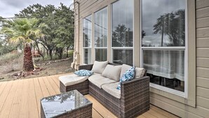 Un porche techado con un sofá de mimbre y una mesa de vidrio, con vistas a un jardín que tiene una palmera y una casa con ventanas grandes.