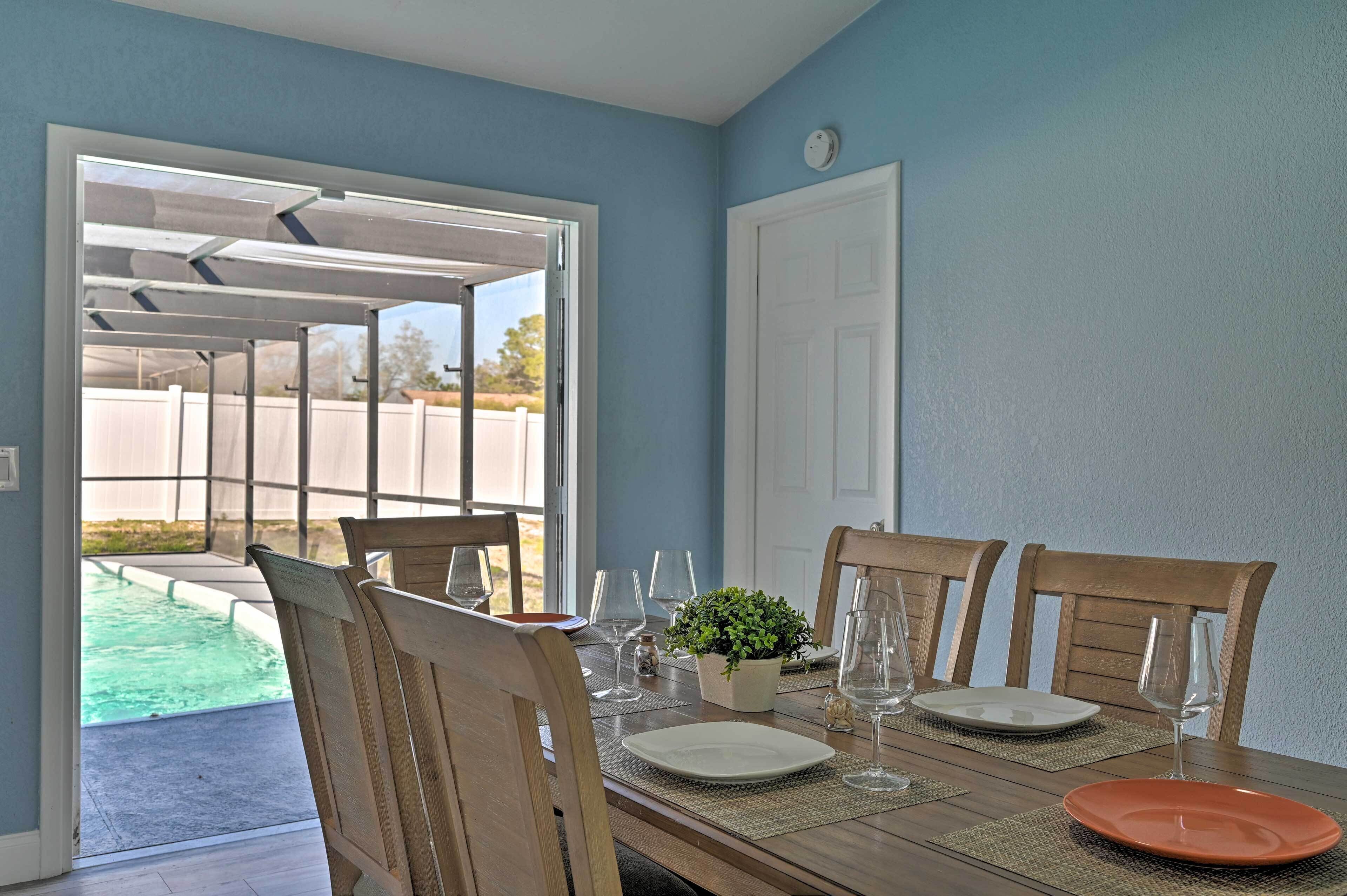 Un comedor con una mesa lista para cuatro personas, una planta en maceta y vista a una piscina.