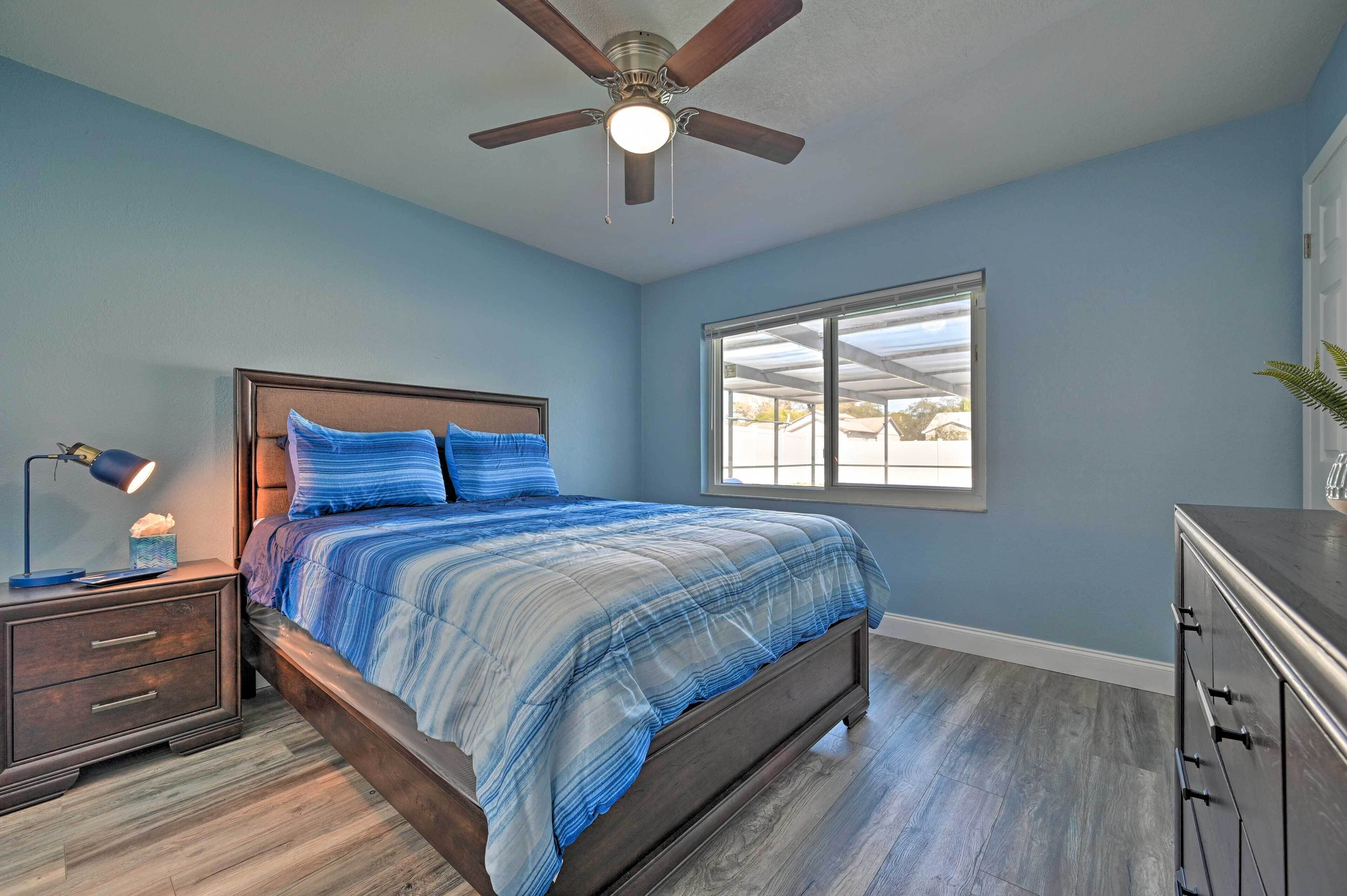 A bedroom with a bed, a nightstand, a dresser, a ceiling fan, and a window.