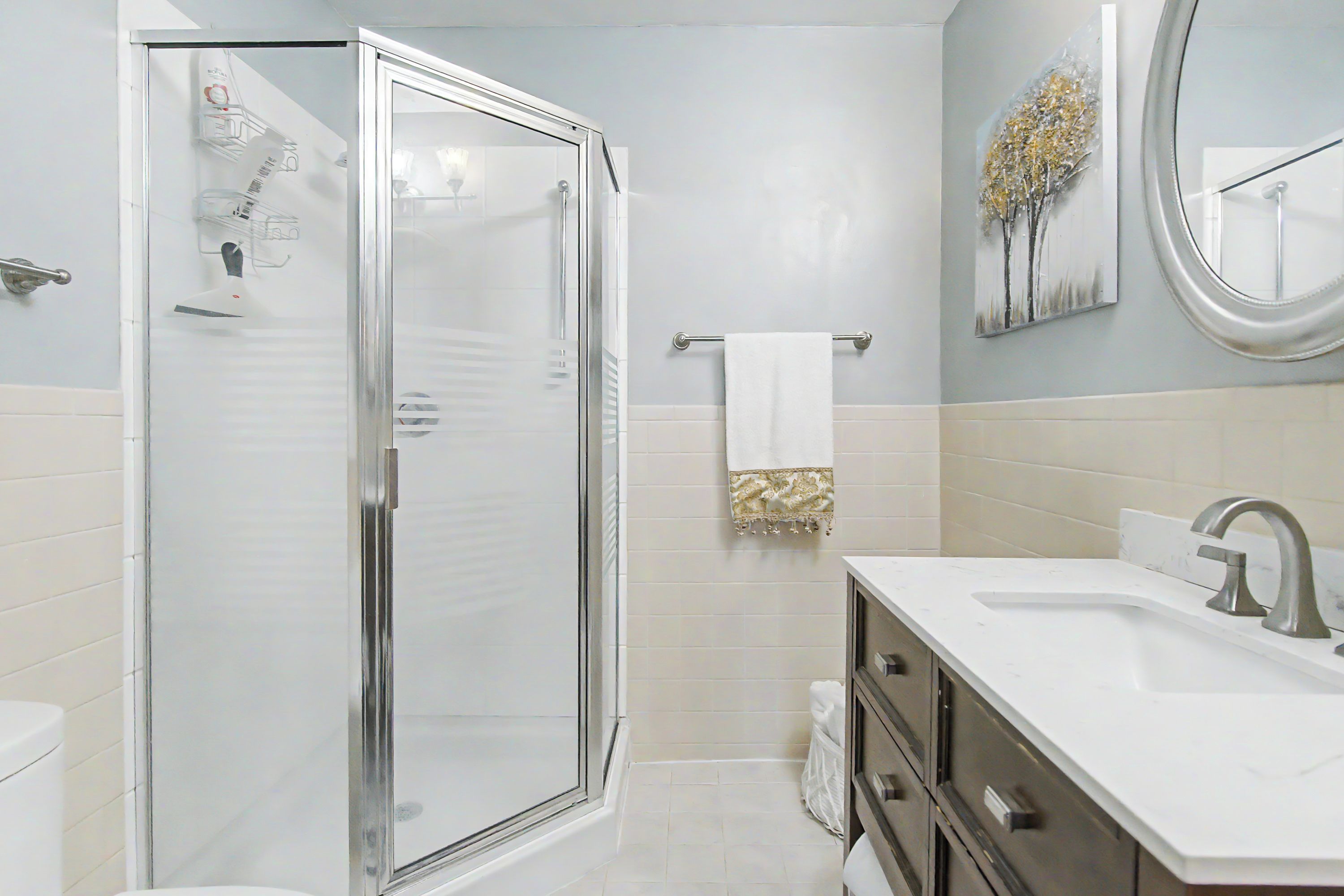 A modern bathroom with a glass-enclosed shower, a white sink with a silver faucet, and a towel rack with a white towel.