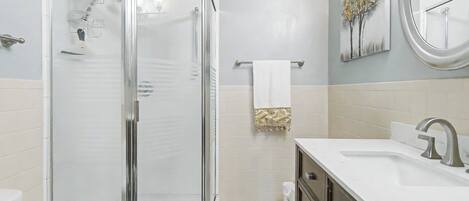 A modern bathroom with a glass-enclosed shower, a white sink with a silver faucet, and a towel rack with a white towel.