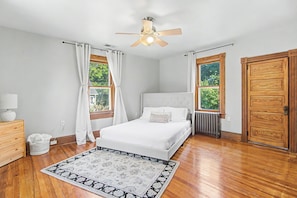 Een slaapkamer met een bed, een plafondventilator, een radiator en een houten deur.