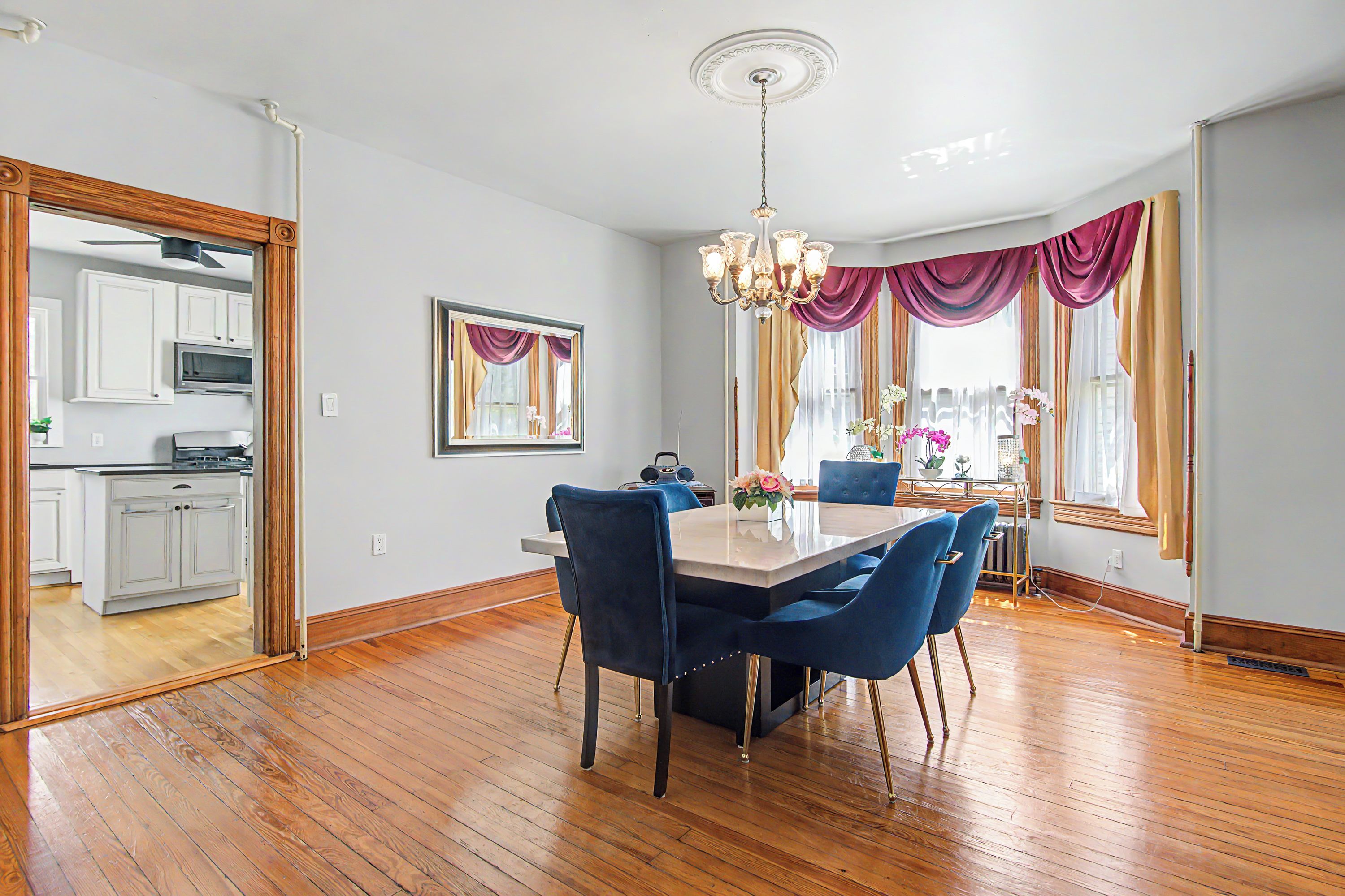 A dining area with a wooden floor, a table with chairs, a chandelier, and a view of the kitchen through an open door.