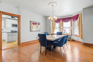 A dining area with a wooden floor, a table with chairs, a chandelier, and a view of the kitchen through an open door. - Front Royal Retreat ~ 1 Mi to National Park! (Front Royal)