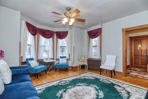 Une pièce avec un canapé bleu, deux fauteuils, une porte en bois et un ventilateur de plafond.