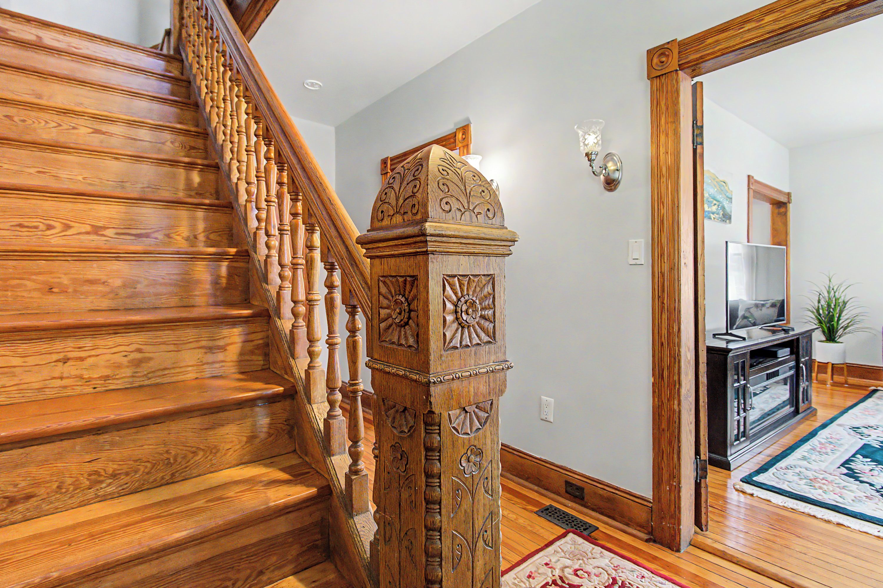 A wooden staircase with intricate carvings, leading to a living area with a television and a plant.