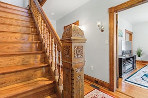 A wooden staircase with intricate carvings, leading to a living area with a television and a plant.