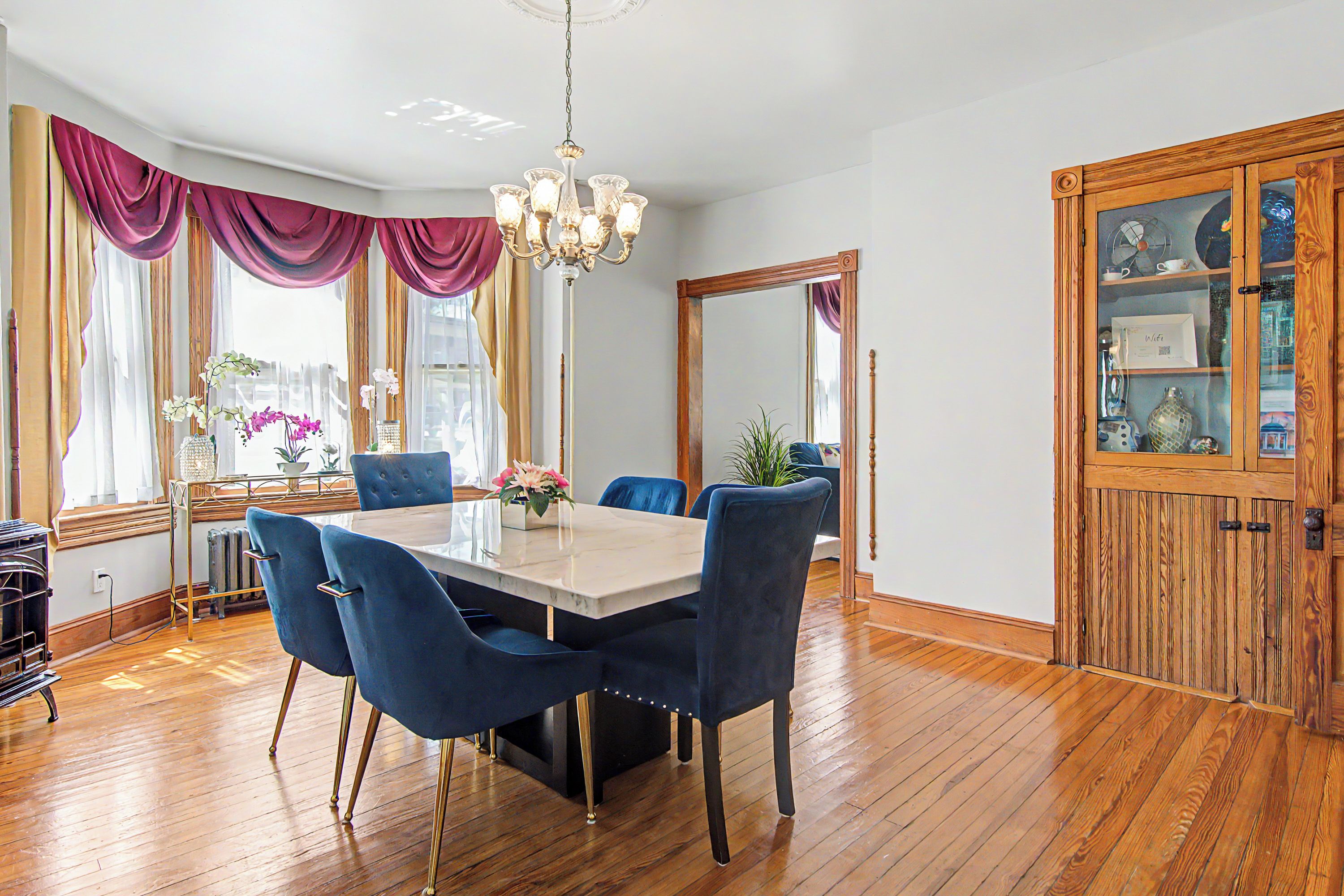 A dining area with a marble table, blue upholstered chairs, and a chandelier.