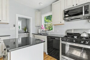 A modern kitchen with white cabinetry, a black countertop, a stainless steel stove, and a built-in dishwasher.