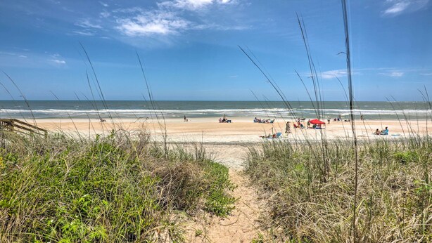 Une plage avec une promenade en bois menant au rivage, une plage de sable et l’océan.