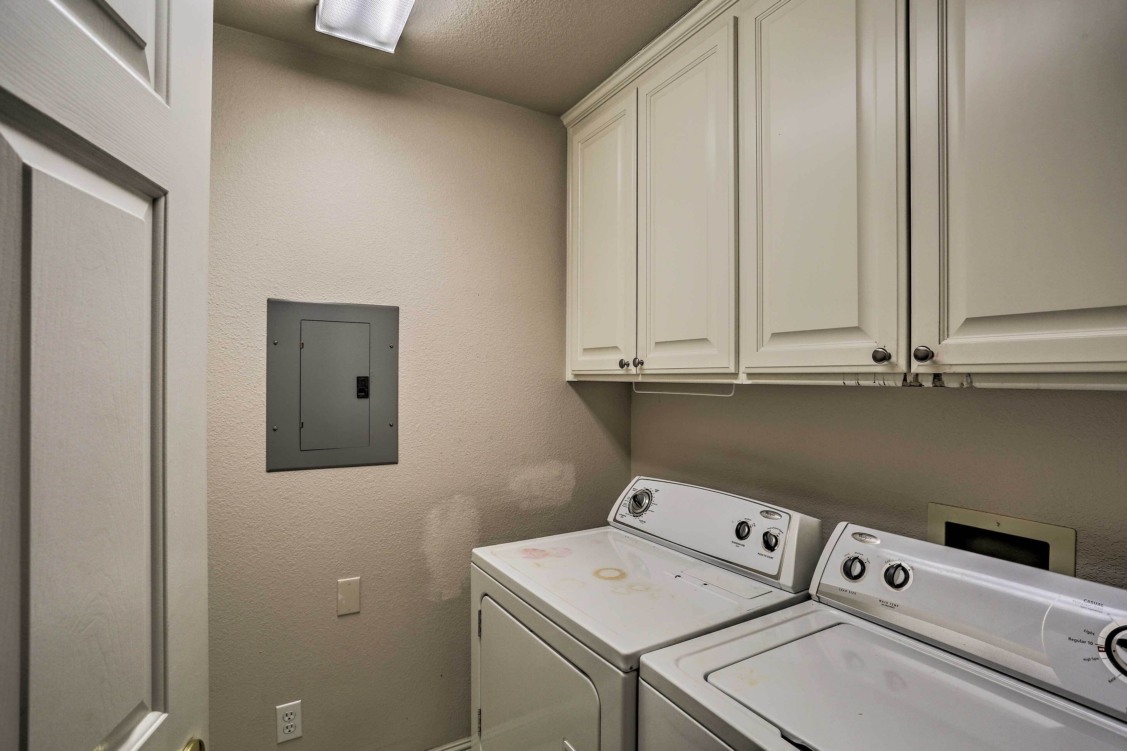 A laundry room with white cabinets, a utility panel, and two stacked washers and dryers.