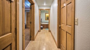 A narrow hallway with wooden doors on both sides, leading to a bathroom with a sink and mirror.