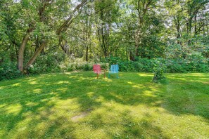 A grassy area with two Adirondack chairs, surrounded by trees and greenery.