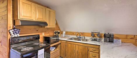 A compact kitchen with wooden cabinets, a stove, a sink, and a marble countertop.