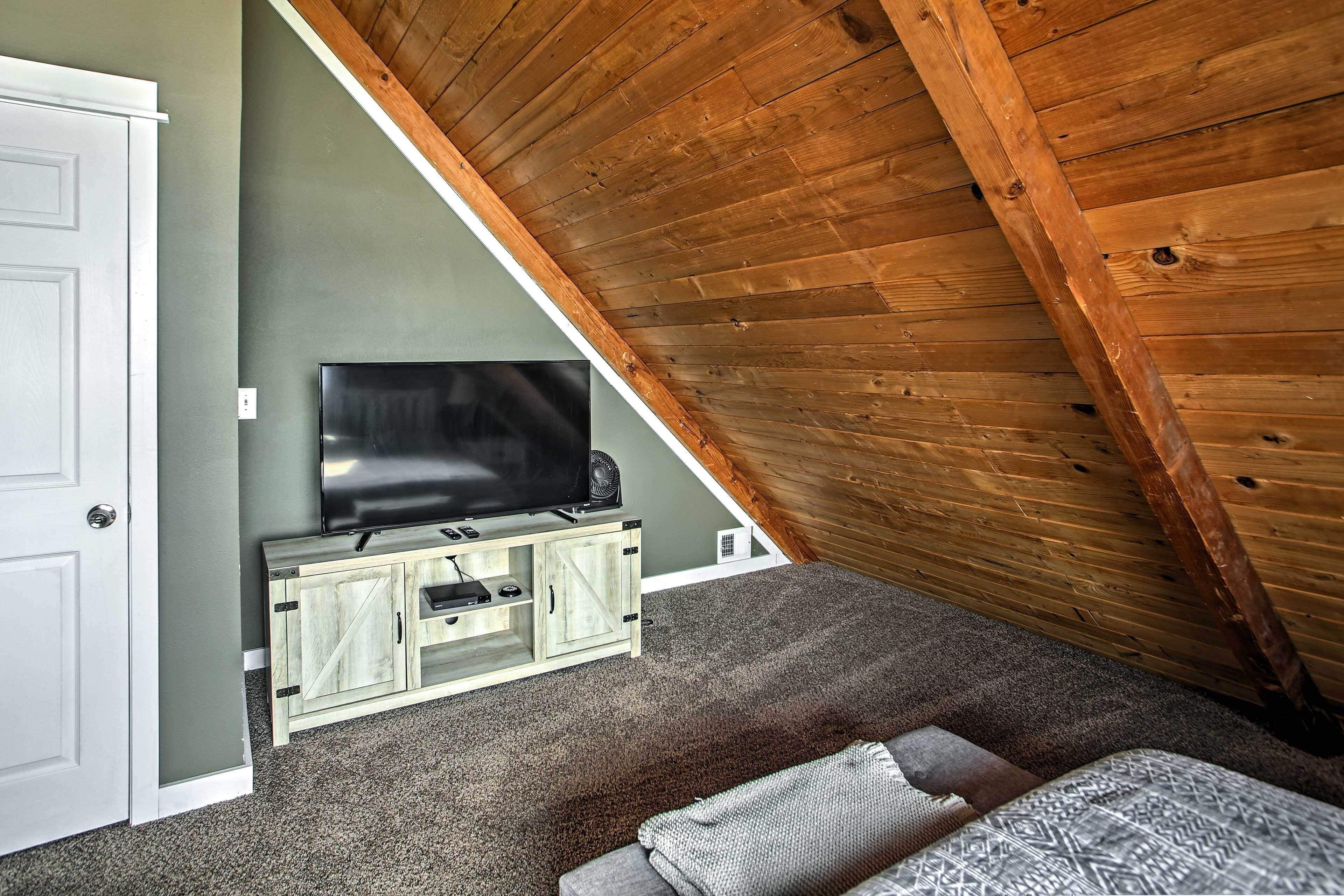 Une pièce avec un plafond en pente, un téléviseur posé sur un meuble en bois, une porte et un sol recouvert de moquette.