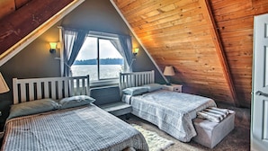 A cozy cabin bedroom with two beds, a large window with curtains, and a view of the water.