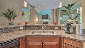 A kitchen with granite countertops, a stainless steel sink, wooden cabinets, a coffee maker, and a ceiling fan.