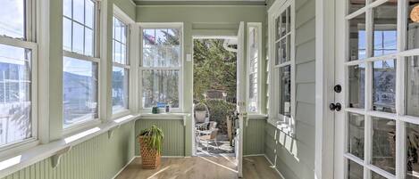 A sunlit corridor with large windows, a wooden floor, and a view of the outside garden.