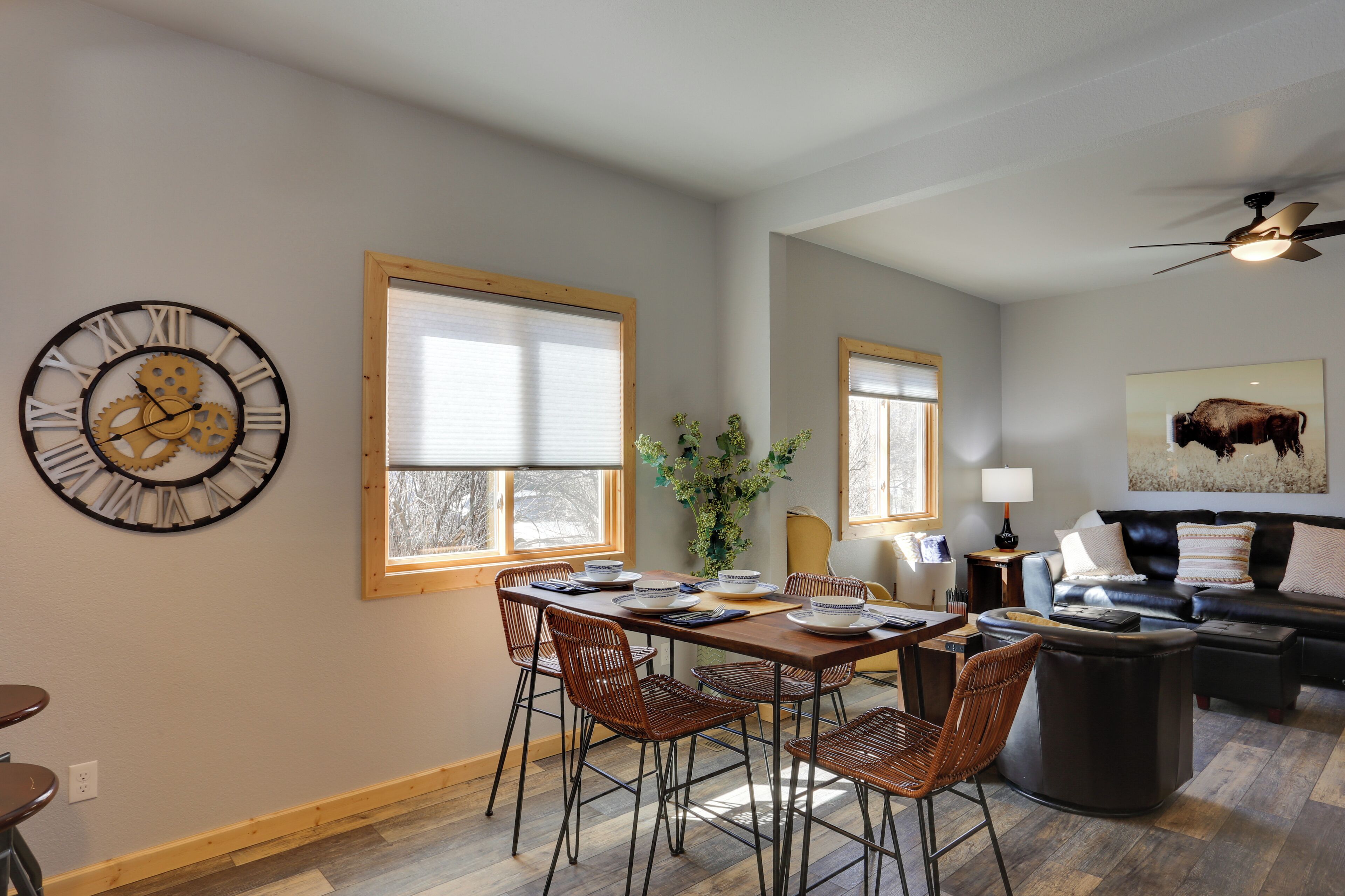 A dining area with a wooden table and chairs, a wall clock, and a window with blinds.