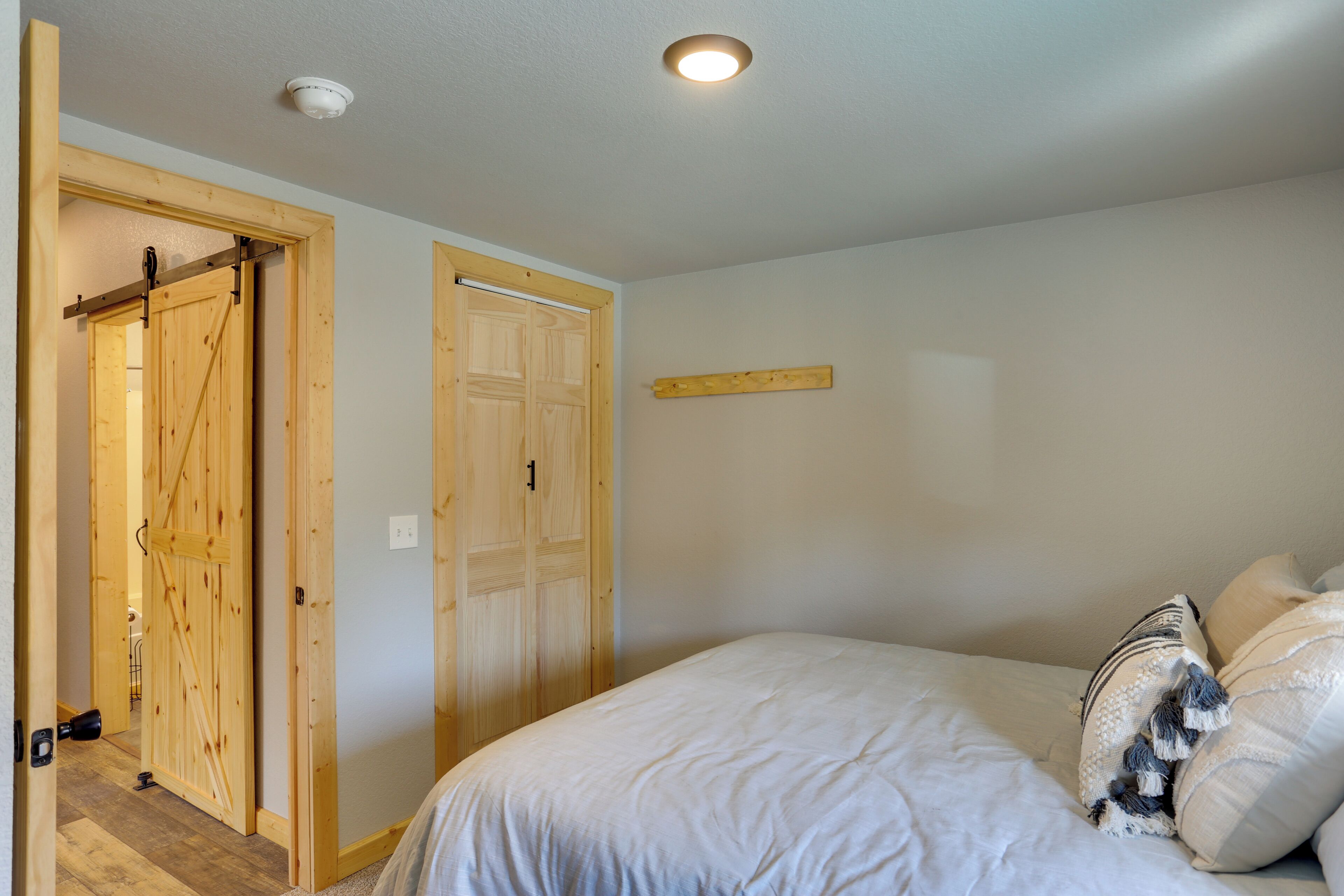 A bedroom with a bed, wooden doors, a ceiling light, and a wall-mounted shelf.