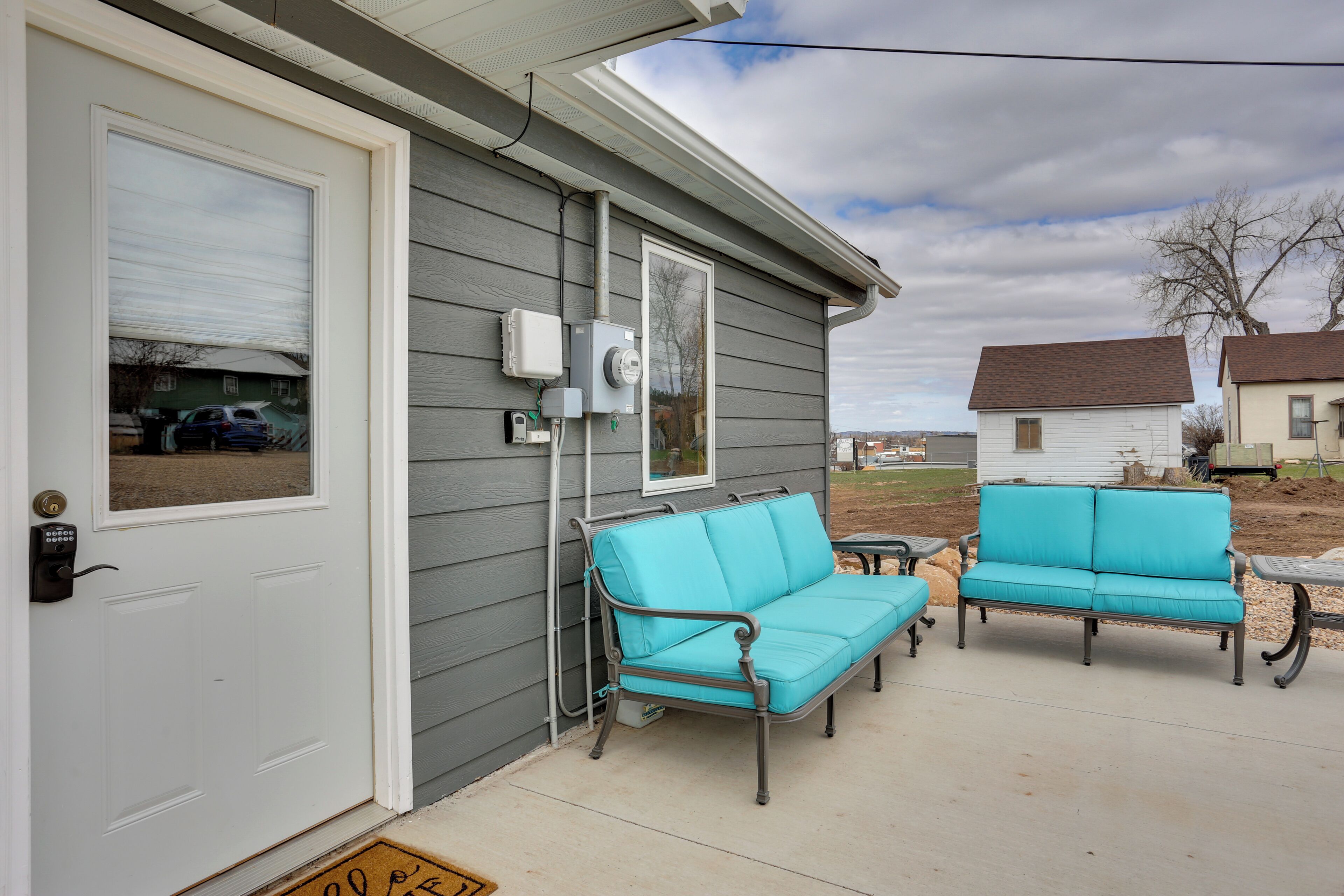 A house with a grey exterior, a white door, and a porch with two turquoise outdoor sofas.