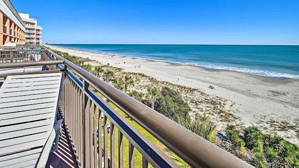 Vista sulla spiaggia da un balcone con ringhiera in legno, che si affaccia su una spiaggia sabbiosa e l'oceano.