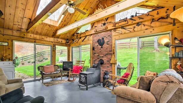 A cozy living room with a fireplace, large windows, and rustic wooden beams. - Scenic Canton Home w/ Sunroom - Near Asheville! (Canton)