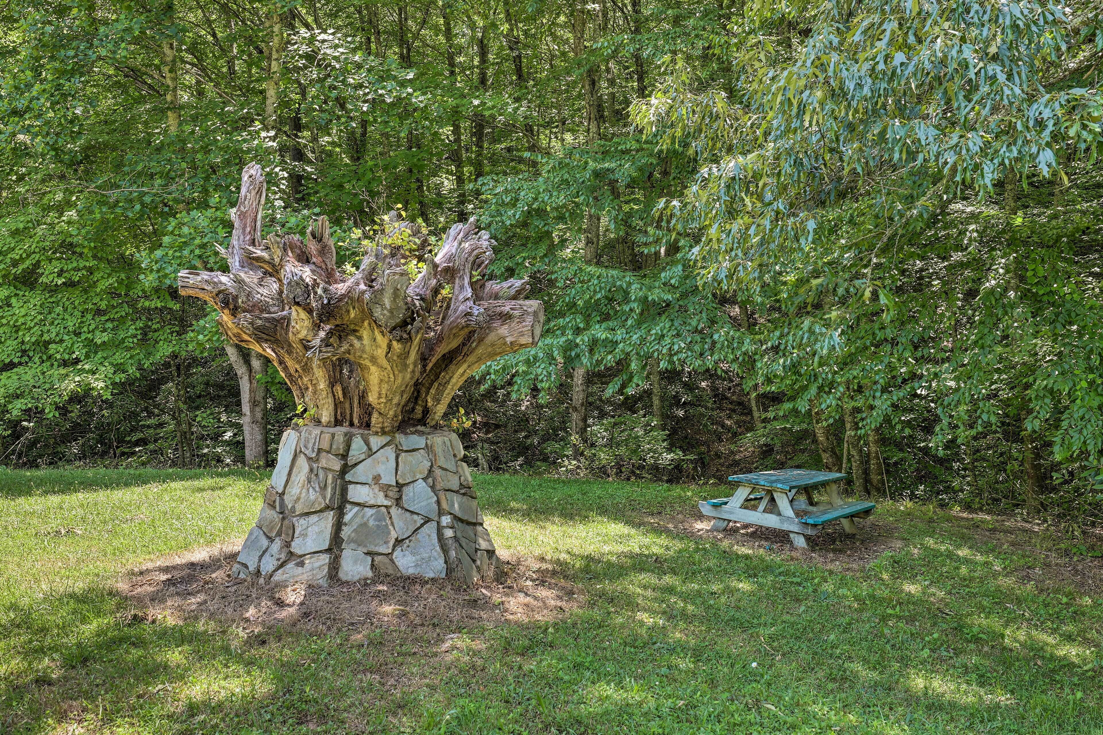 A stone planter with a tree trunk and a picnic table in a forested area.