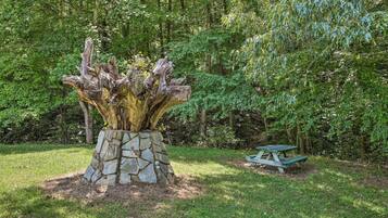 A stone planter with a tree trunk and a picnic table in a forested area.