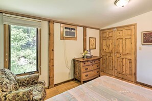 A bedroom with a bed, a wooden dresser, a window with blinds, and a door.