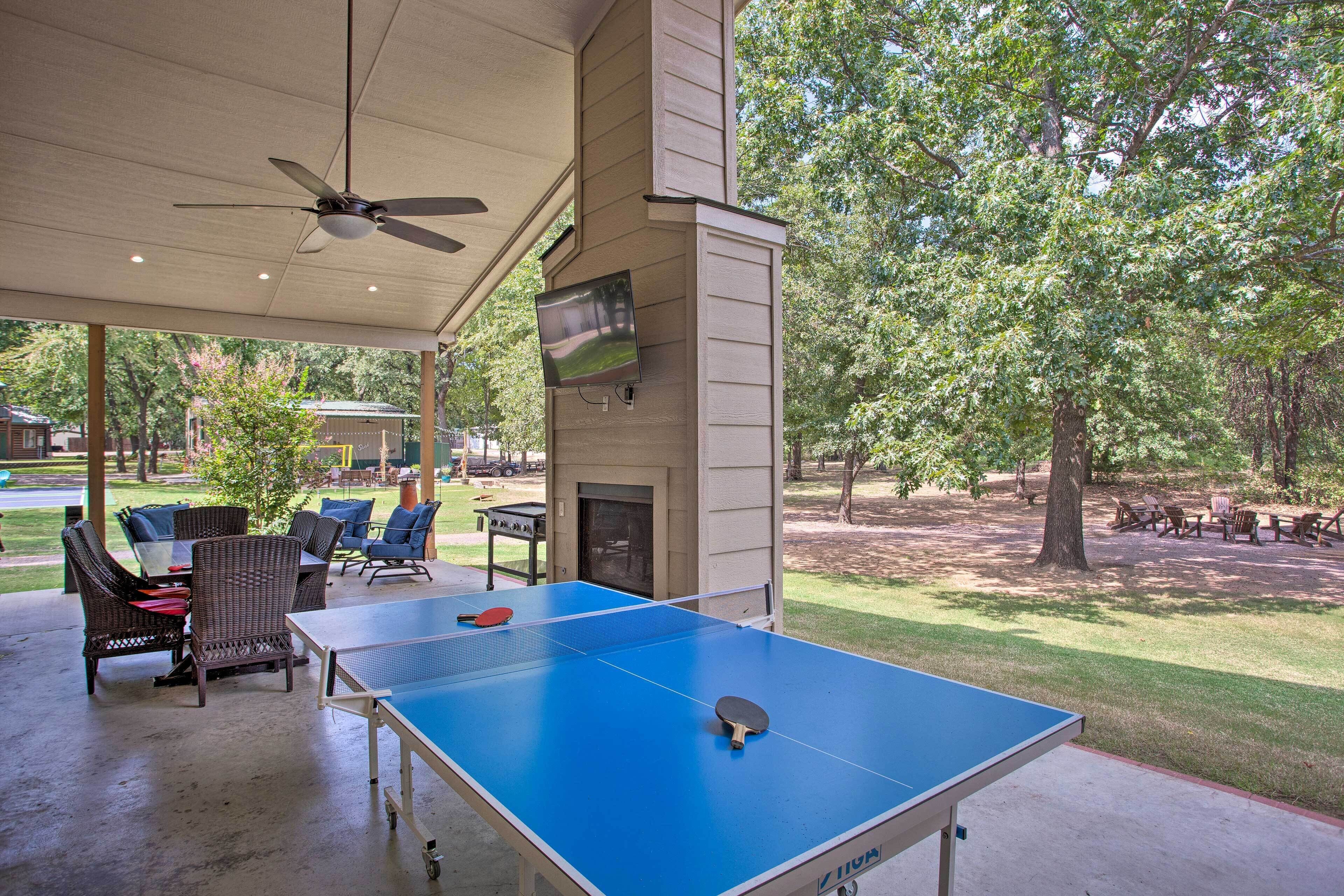An outdoor ping pong table with a ceiling fan, seating area, and a TV mounted on the wall.