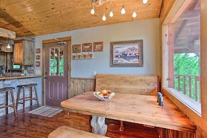 A wooden dining table with a bowl of fruit, a bench, and a window with a view of greenery. - Beautiful Country Cabin on Crooked Creek Farm! (Carnegie)