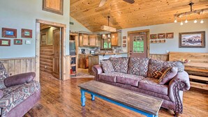 A cozy living room with a wooden ceiling, a sofa, a coffee table, and a kitchen in the background. - Beautiful Country Cabin on Crooked Creek Farm! (Carnegie)