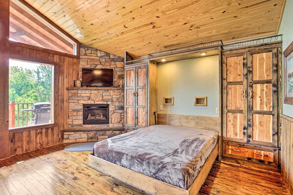 A bedroom with a stone fireplace, wooden ceiling, and a large bed.