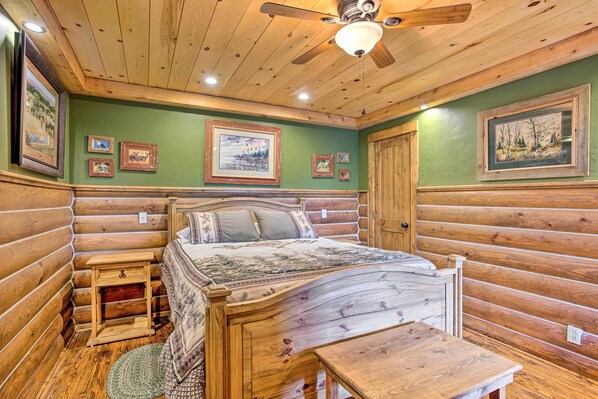 A log cabin-style bedroom with a wooden bed, a nightstand, a small table, and a ceiling fan.