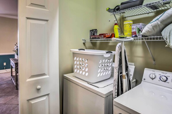 A laundry area with a washing machine, a dryer, and a shelf with cleaning supplies. - Myrtle Beach Condo: Pool & Golf Course Access (Myrtle Beach)