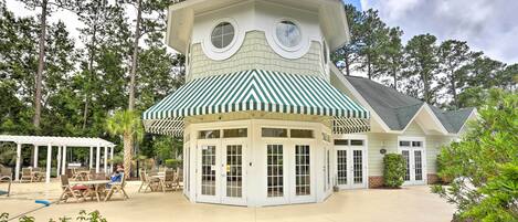 A unique building with a rounded tower and a green-striped awning, surrounded by trees and outdoor seating.