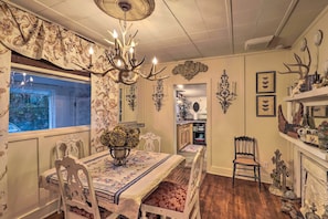 Comedor con candelabro, papel tapiz floral y vista a la cocina.