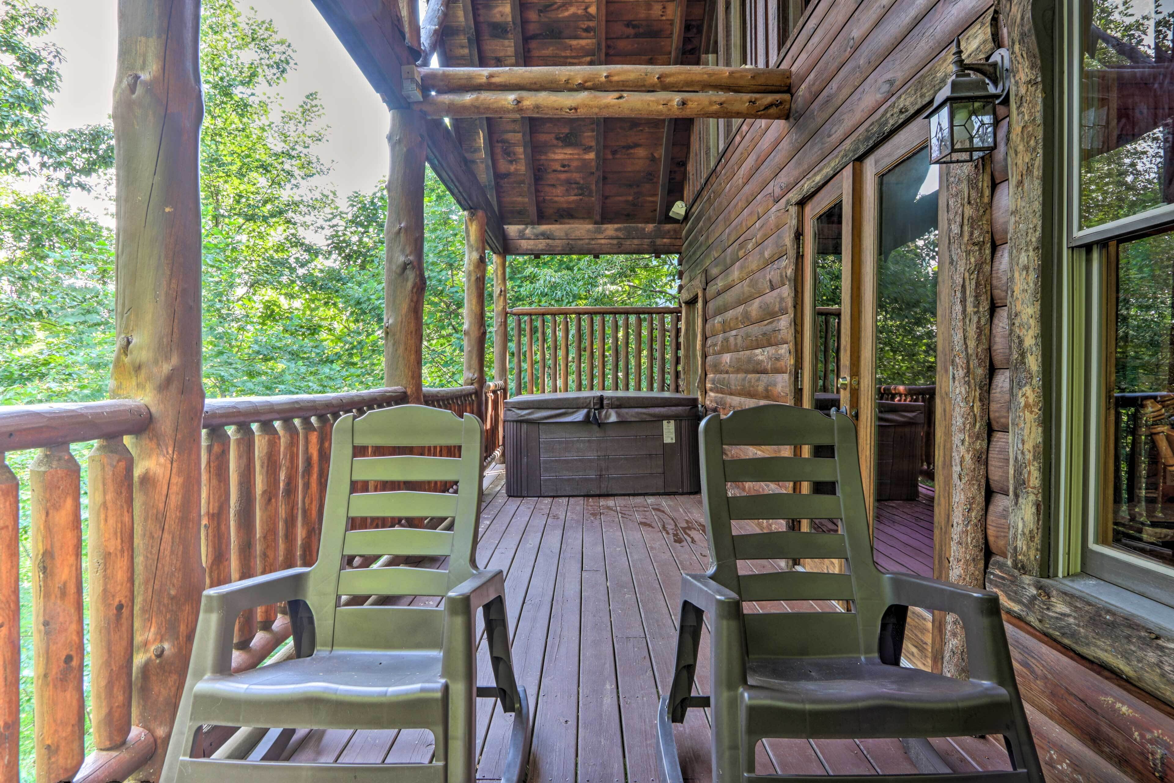 Een houten terras met twee groene stoelen, een jacuzzi en een houten leuning.