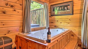 A wooden cabin bathroom with a bathtub, a wine bottle, and a framed picture of horses. - 'sky Harbor' Sevierville Cabin w/ Hot Tub & Deck! (Sevierville)