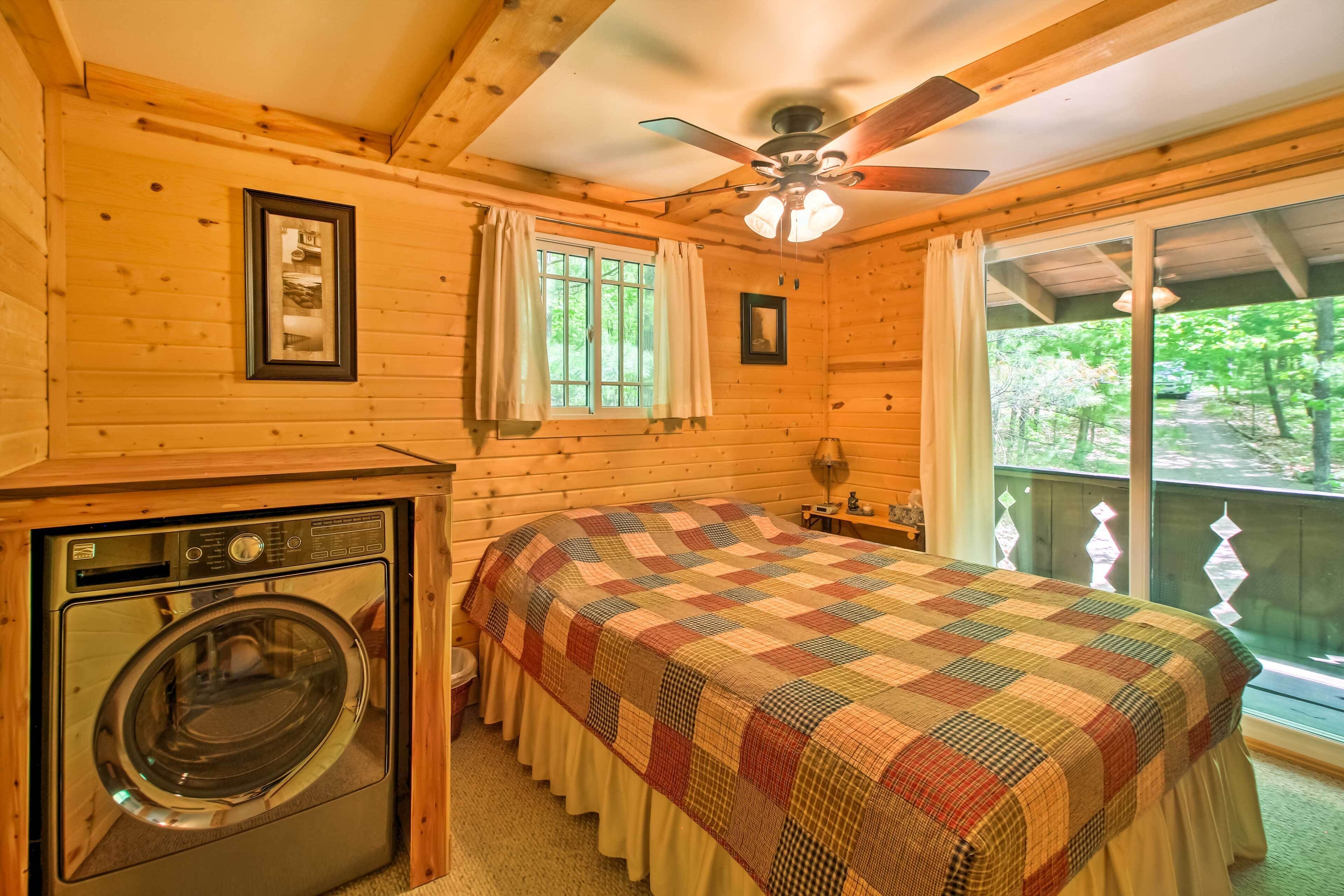 A wooden cabin room with a bed, a ceiling fan, a window with curtains, and a washing machine.