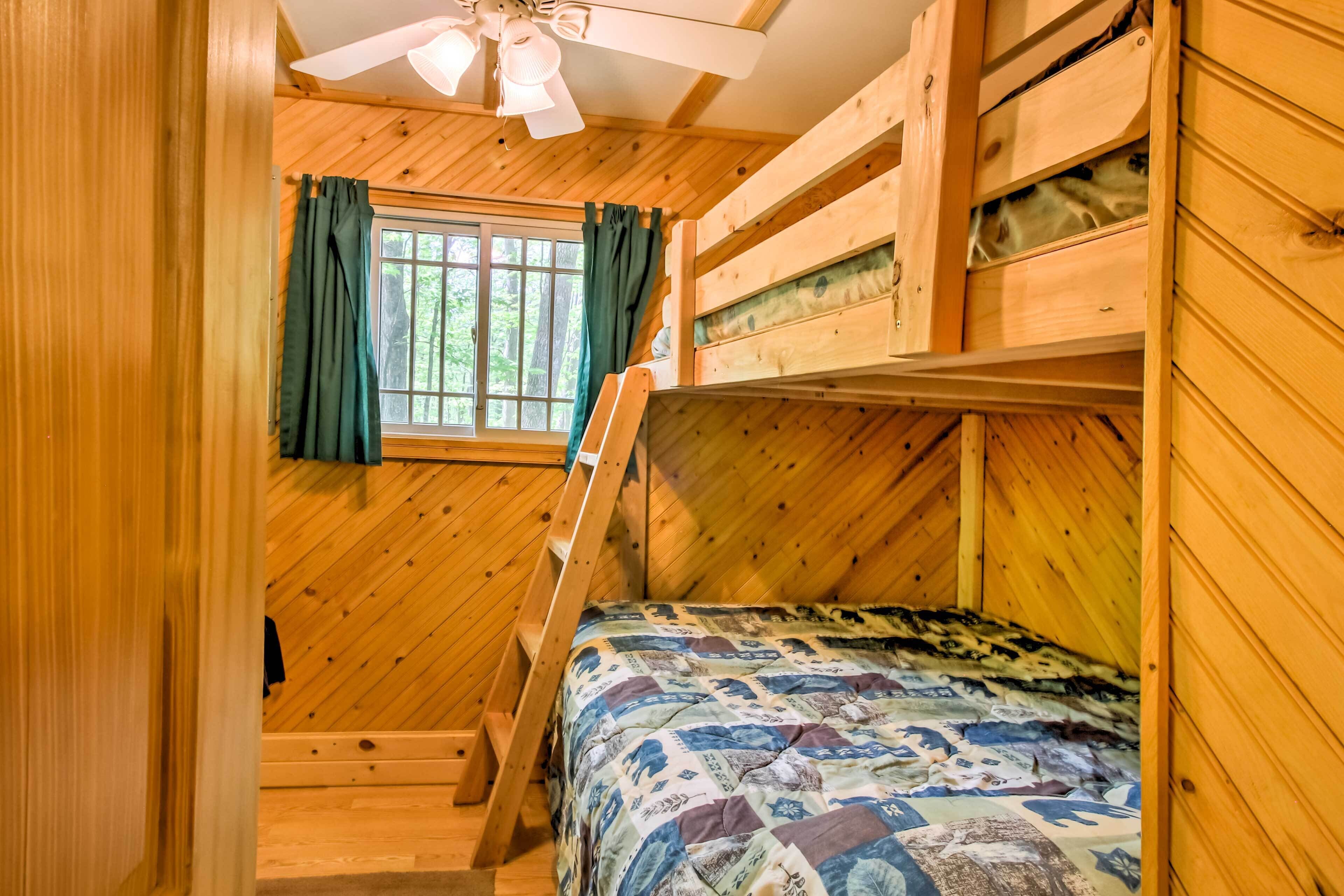 A wooden cabin bedroom with bunk beds, a window with curtains, and a ceiling fan.