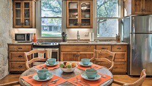 A kitchen with wooden cabinets, a stainless steel refrigerator, and a dining table set with blue bowls and plates. - Blanco Riverfront Historic Home, 3 Mi to Downtown! (Blanco)